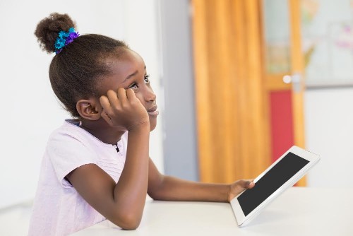 Thoughtful schoolgirl with digital tablet in classroom at school