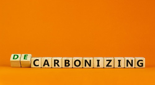 Carbonizing or decarbonizing symbol. Turned wooden cubes and changed words 'carbonizing' to 'decarbonizing'. Orange background, copy space. Business, carbonizing or decarbonizing concept.