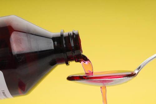 A bottle pouring cough syrup into a spoon with a yellow background