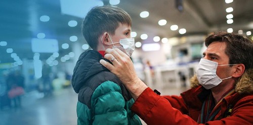 father putting medical mask on his son to protect himself from the coronavirus in an airport terminal or shopping mall
