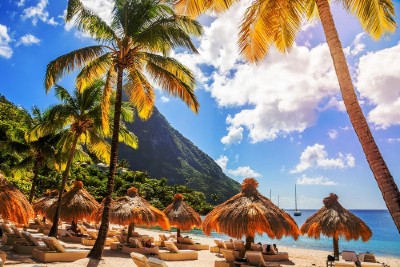 Caribbean beach with palms and straw umrellas on the shore with Gros Piton mountain in the background, Sugar beach, Saint  Lucia