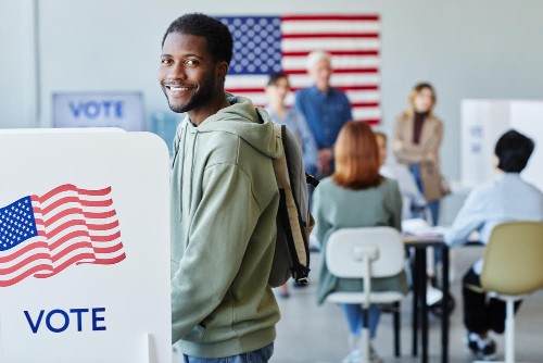 Side view portrait of smiling black man voting in booth on election day and looking at camera, copy space