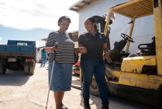 UNDP Assistant Resident Representative Lesley Ann Ennevor (right) supports Villette Neil, a poultry farmer who is blind, in receiving her gift of inputs to recover her poultry business resiliently. She is one of 125 SMEs who have so far received support under JARRI, in partnership with Jamaica 4H, Jamaica Network of Rural Women Producers and the Bureau of Gender Affairs.