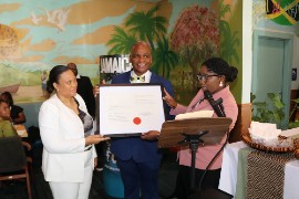 Ms. Lishann Salmon, Chargé d’Affaires, a.i., at the Embassy of Jamaica, formally presents Jamaica’s Honorary Consul to Richmond, Lieutenant Karl M. Bryan, with his Writ of Commission during his installation ceremony at Carena’s Jamaican Grill in Richmond on Sunday, August 23, 2026. At right is Mrs. Chantelle Edwards, Counsellor at the Embassy of Jamaica in Washington, D.C. (Derrick Scott Photo)