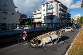A man rides his bicycle past burned cars after violent demonstrations which broke out over coronavirus disease (COVID-19) protocols, in Pointe-a-Pitre, Guadeloupe November 21, 2021. (REUTERS/Ricardo Arduengo)