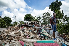 A man stands on top of the debris of crushed houses and a former voodoo community center in the community of Les Cayes. (Photo: WFP/Marianela Gonzaleznr)