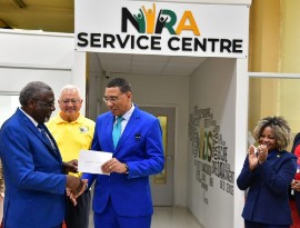 Prime Minister Andrew Holness receives his national ID card from Chairman of the National Identification Registration Authority, Bishop Conrad Pitkin (left). Looking on are Justice Minister Delroy Chuck (second left) and Minister of Education, Skills, Youth and Information, Senator Dr. Dana Morris Dixon (right) who also received their cards.
